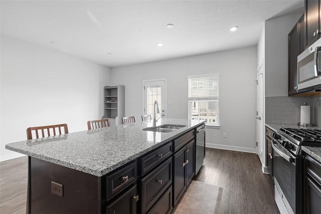 kitchen featuring dark wood finished floors, a sink, decorative backsplash, a center island with sink, and appliances with stainless steel finishes