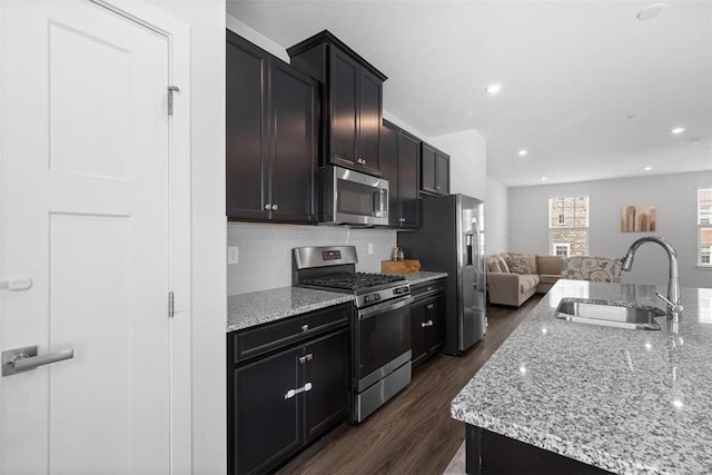 kitchen with a sink, open floor plan, dark wood-type flooring, appliances with stainless steel finishes, and decorative backsplash