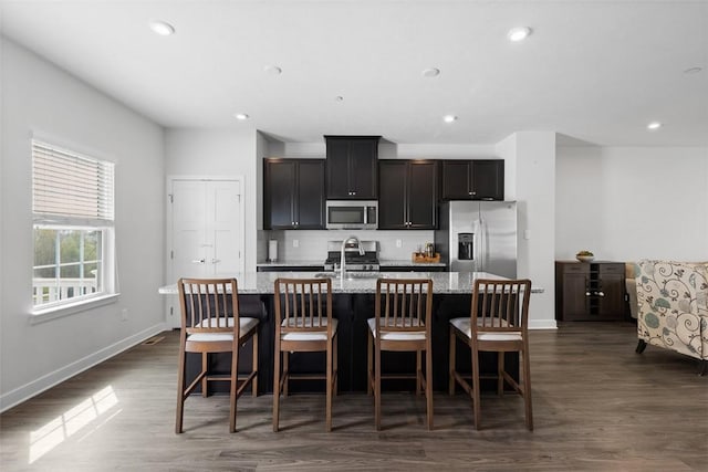 kitchen with stainless steel appliances, baseboards, recessed lighting, and a center island with sink