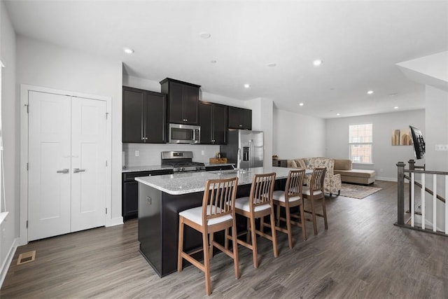 kitchen featuring wood finished floors, an island with sink, visible vents, appliances with stainless steel finishes, and dark cabinetry