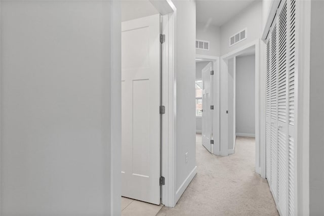 hallway featuring light colored carpet, baseboards, and visible vents