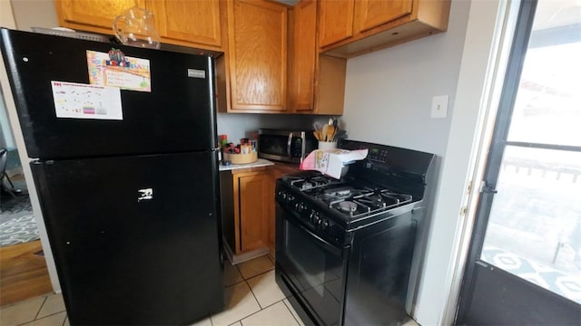 kitchen with light tile patterned floors, brown cabinetry, and black appliances