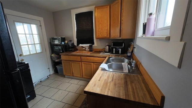 kitchen with wood counters, light tile patterned flooring, a sink, and brown cabinets