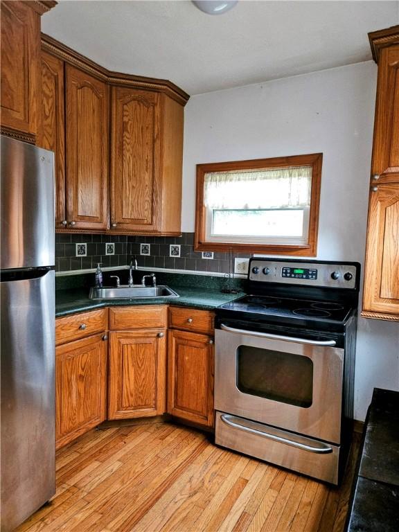 kitchen with a sink, appliances with stainless steel finishes, light wood-style floors, and dark countertops
