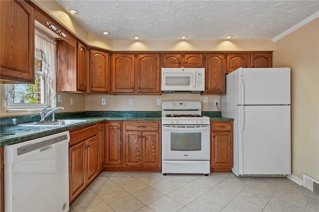 kitchen with white appliances, brown cabinets, dark countertops, and a sink