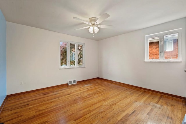 empty room featuring visible vents, a ceiling fan, light wood-style floors, and baseboards