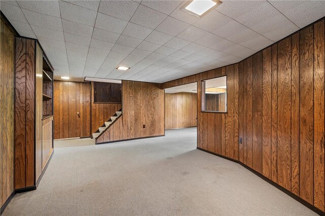 finished basement featuring baseboards, carpet, wooden walls, and stairway