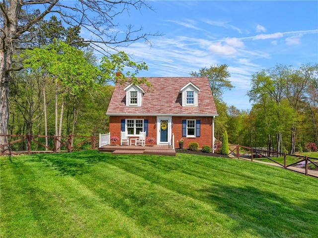 cape cod home featuring a chimney, a wooden deck, a front yard, a fenced backyard, and brick siding