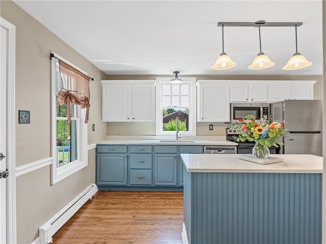 kitchen with a sink, stainless steel appliances, a baseboard heating unit, light wood-style floors, and blue cabinetry