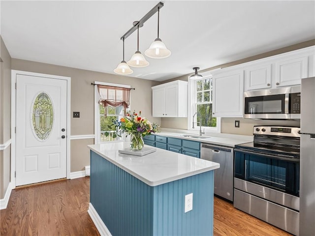 kitchen with stainless steel appliances, light wood finished floors, a sink, light countertops, and white cabinets
