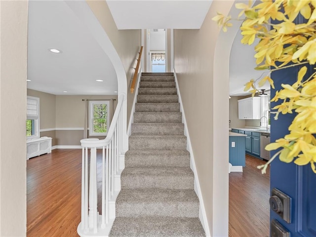 stairway with wood finished floors, baseboards, arched walkways, and recessed lighting