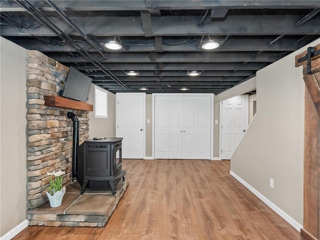 basement with baseboards, a wood stove, and wood finished floors