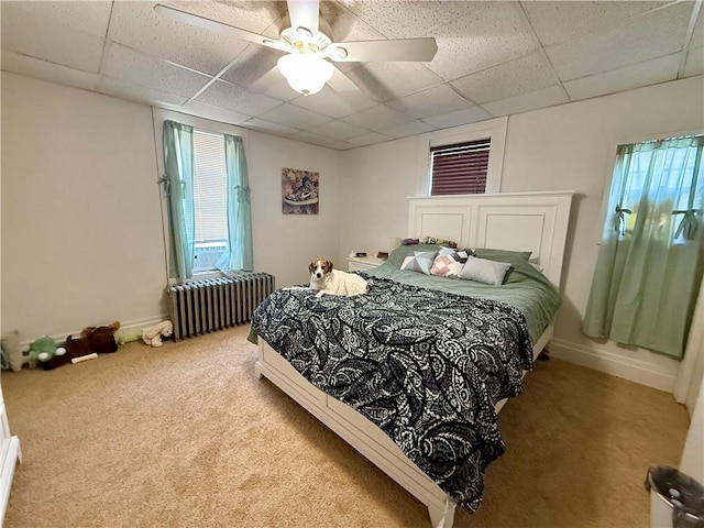 carpeted bedroom featuring a drop ceiling, a ceiling fan, multiple windows, and radiator heating unit