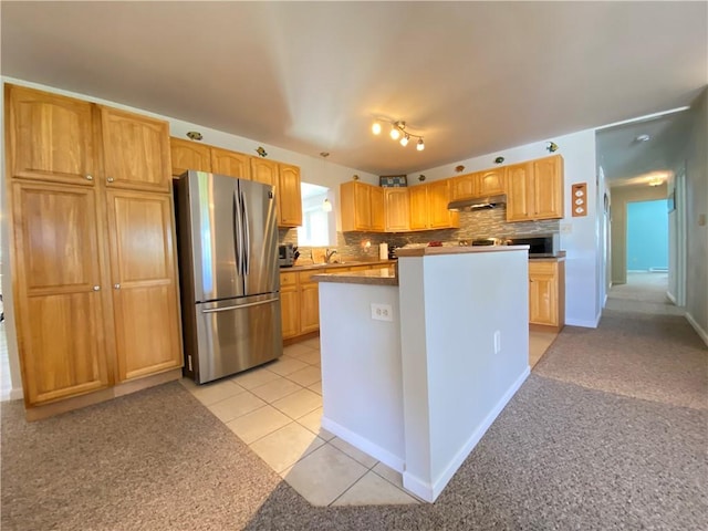 kitchen with freestanding refrigerator, under cabinet range hood, light carpet, backsplash, and a kitchen island