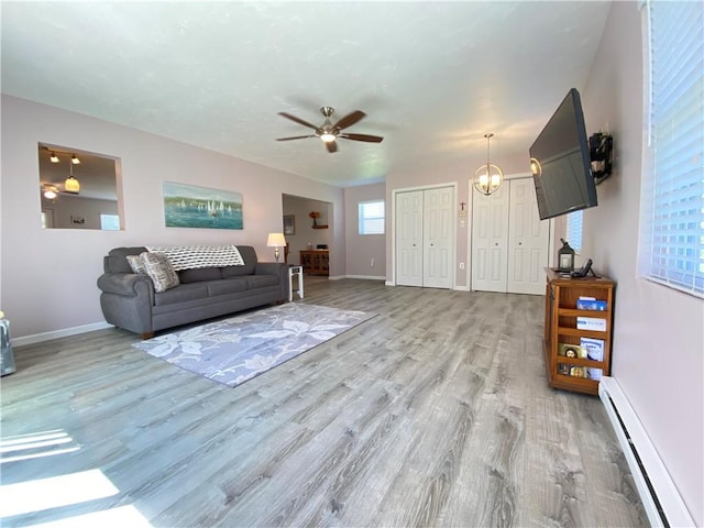 living room with ceiling fan with notable chandelier, baseboards, light wood-type flooring, and a baseboard heating unit