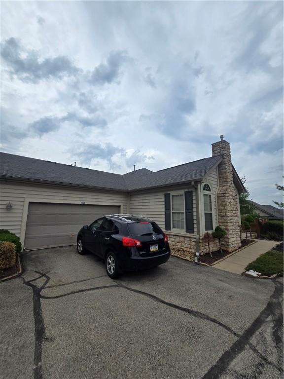view of front of home featuring aphalt driveway, stone siding, an attached garage, and a chimney