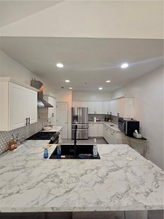 kitchen with a sink, a peninsula, wall chimney exhaust hood, black appliances, and white cabinets