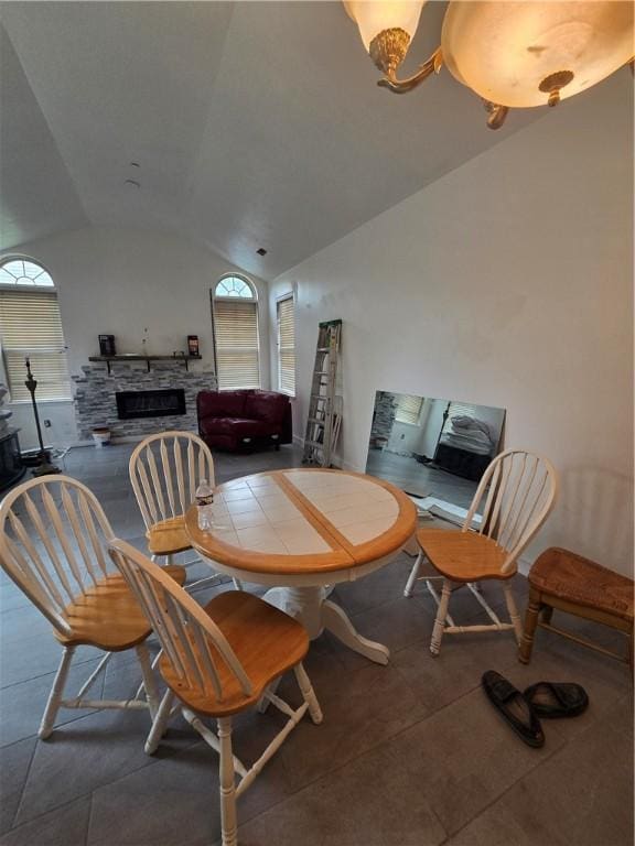 dining area featuring tile patterned flooring, lofted ceiling, and a stone fireplace