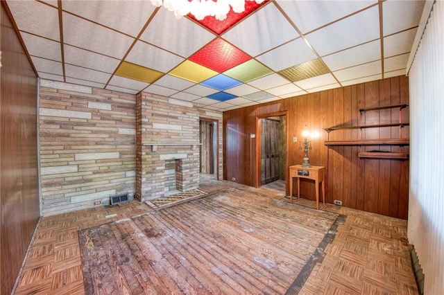 unfurnished living room featuring a large fireplace, wooden walls, visible vents, and a paneled ceiling