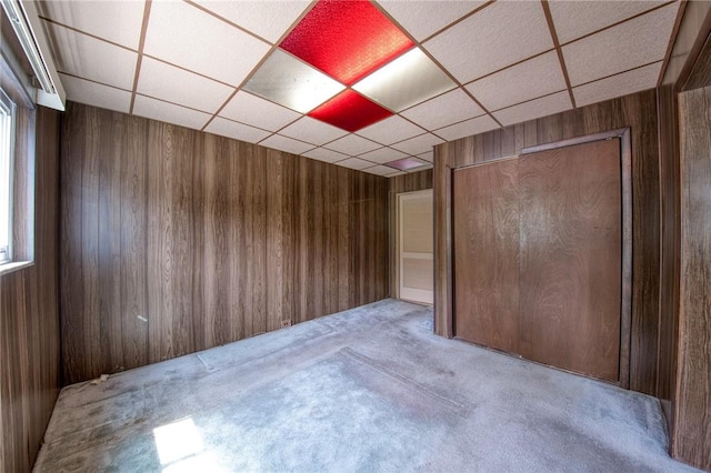 spare room featuring carpet flooring, a drop ceiling, and wood walls