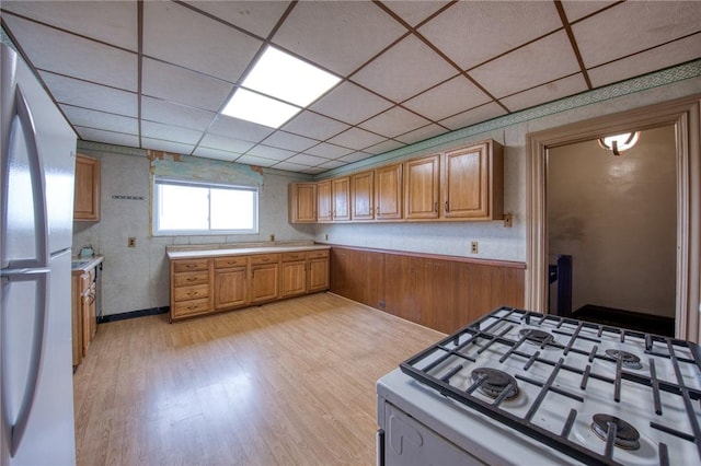 kitchen with white range with gas cooktop, brown cabinets, freestanding refrigerator, light wood finished floors, and light countertops