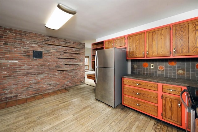 kitchen featuring freestanding refrigerator, range, brown cabinets, tile counters, and light wood-style floors