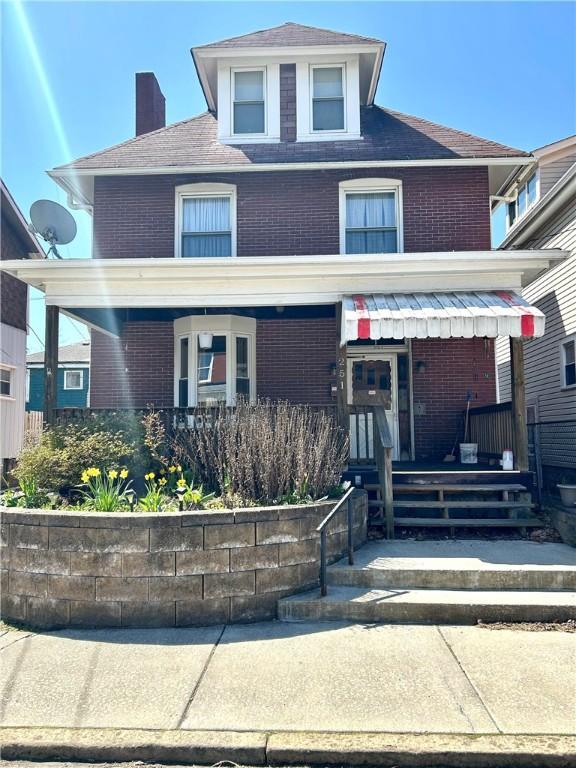 american foursquare style home with covered porch, a chimney, and brick siding