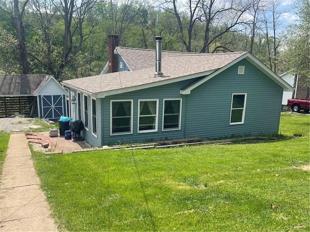 rear view of property with a chimney, roof with shingles, a storage shed, and a lawn