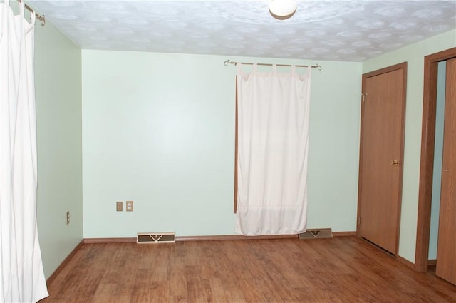 unfurnished bedroom featuring baseboards, visible vents, two closets, and wood finished floors