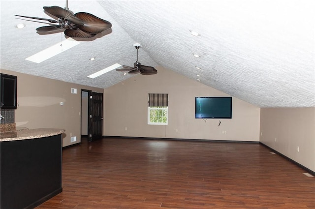 unfurnished living room with ceiling fan, lofted ceiling with skylight, baseboards, and wood finished floors