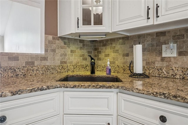 kitchen with a sink, white cabinets, dark stone counters, and tasteful backsplash