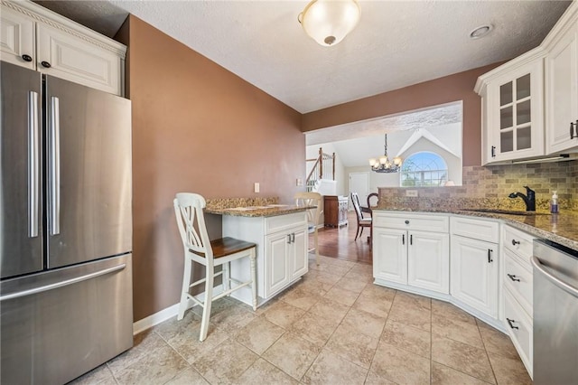 kitchen with appliances with stainless steel finishes, a peninsula, lofted ceiling, a sink, and a chandelier