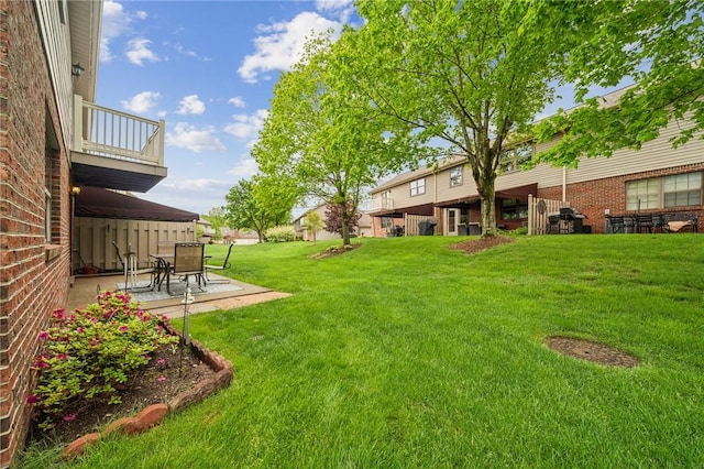 view of grassy yard with a balcony and a patio