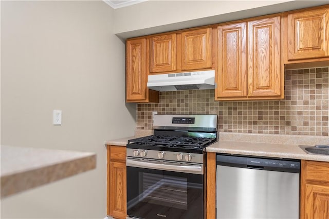 kitchen with under cabinet range hood, stainless steel appliances, tasteful backsplash, and light countertops