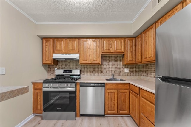 kitchen featuring a sink, stainless steel appliances, under cabinet range hood, light wood-style flooring, and light countertops