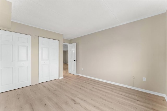 unfurnished bedroom with light wood finished floors, ornamental molding, baseboards, and multiple closets
