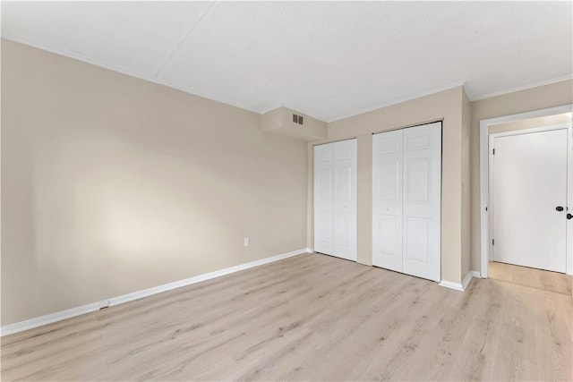 unfurnished bedroom featuring wood finished floors, visible vents, two closets, crown molding, and baseboards