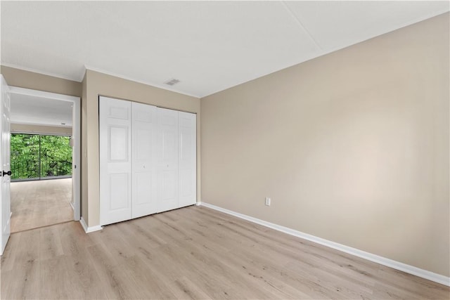 unfurnished bedroom featuring a closet, crown molding, light wood-type flooring, visible vents, and baseboards