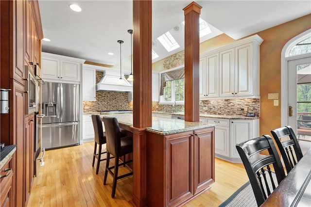 kitchen featuring light wood-style flooring, tasteful backsplash, stainless steel refrigerator with ice dispenser, and decorative columns