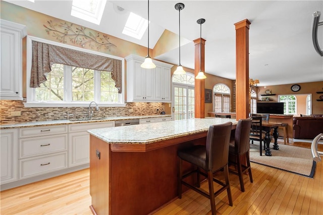 kitchen featuring light wood finished floors, a center island, a sink, a skylight, and light stone countertops