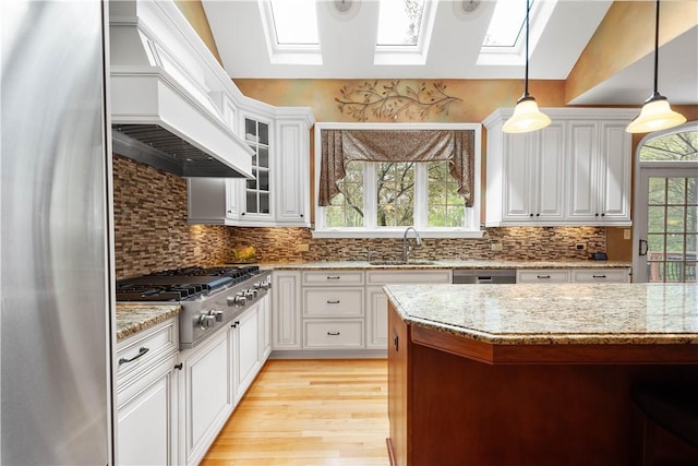 kitchen featuring stainless steel appliances, a skylight, white cabinetry, light wood-style floors, and custom range hood