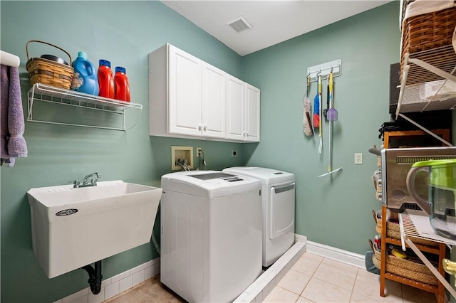 laundry area featuring a sink, cabinet space, separate washer and dryer, light tile patterned floors, and baseboards
