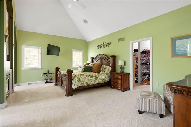 bedroom featuring a ceiling fan, high vaulted ceiling, a walk in closet, visible vents, and light carpet