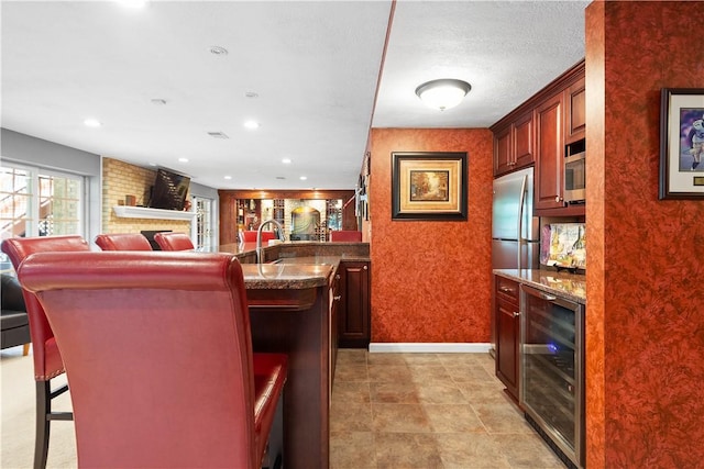 kitchen with a breakfast bar, a center island with sink, open floor plan, beverage cooler, and appliances with stainless steel finishes