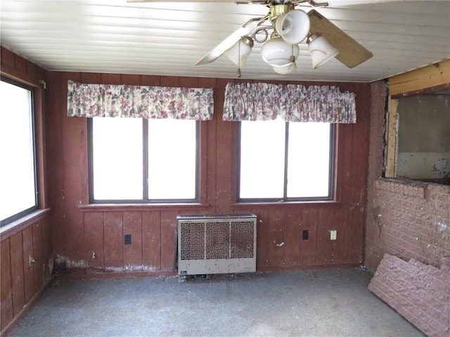 unfurnished room featuring wood walls, a ceiling fan, and radiator heating unit