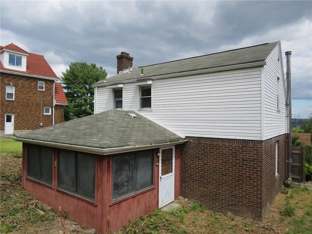 back of property featuring a sunroom, brick siding, roof with shingles, and a chimney