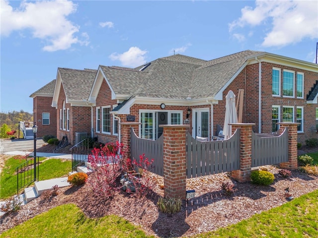 view of front of property featuring roof with shingles, brick siding, and fence