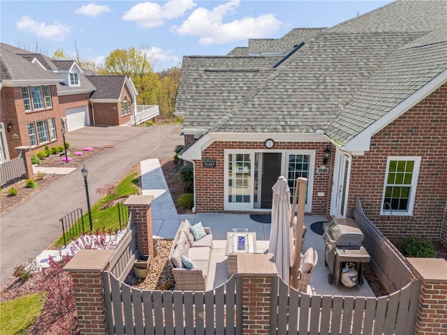 exterior space with a fenced front yard, roof with shingles, a garage, and brick siding