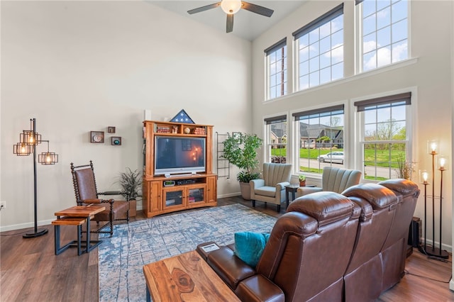 living room featuring baseboards, wood finished floors, a towering ceiling, and ceiling fan