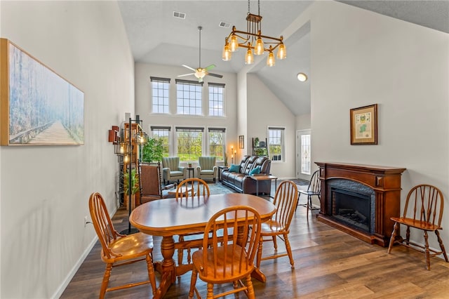 dining room with a high end fireplace, wood finished floors, high vaulted ceiling, and ceiling fan with notable chandelier